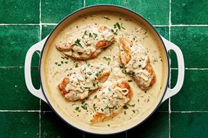 Four browned chicken breasts in a creamy tarragon sauce topped with black pepper and fresh tarragon leaves.