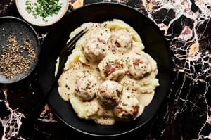 a bowl of homemade turkey meatballs in cream sauce served on top of mashed potatoes and sprinkled with fresh parsley