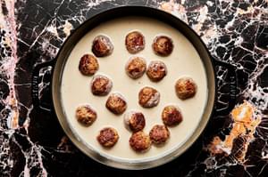 turkey meatballs being cooked in cream sauce in a skillet