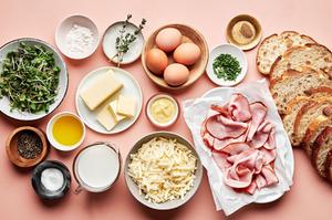 bread, ham, Gruyère, eggs, butter, chives, micro greens and ingredients for homemade Béchamel sauce in prep bowls