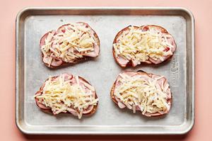 buttered bread toped with slices of ham and Gruyère on a baking sheet