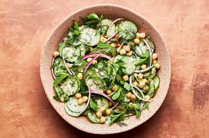 cucumber salad being tossed with homemade dressing in a large bowl