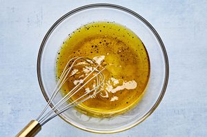 olive oil, rice wine vinegar, honey, salt and pepper being whisked in a bowl