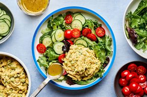 salad greens topped with cucumbers, tomatoes and curried chicken salad being drizzled with homemade dressing