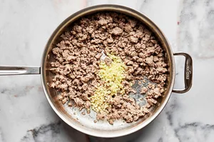 ginger, garlic and ground pork being cooked in vegetable oil in a skillet