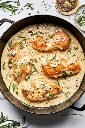 dijon chicken in a skillet made with cream, wine, dijon and sprinkled with pepper and fresh tarragon