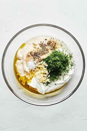 olive oil, mayo, sour cream, garlic, dill, garlic powder, onion powder, lemon juice, salt & pepper being mixed in a bowl