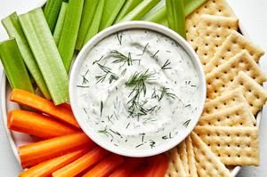 homemade dill dip in a bowl on a serving platter surrounded by celery, carrots and crackers for dipping