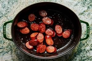 sliced beef sausage being cooked in bacon fat in a dutch oven pot