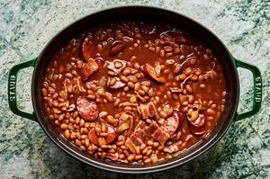 baked beans, maple syrup, mustard, molasses, ketchup, vinegar, bacon sausage and onion being stirred together in a dutch oven