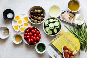Ingredients laid out for easy nicoise salad potatoes, tuna fish, tomatoes, olives and soft boiled eggs.