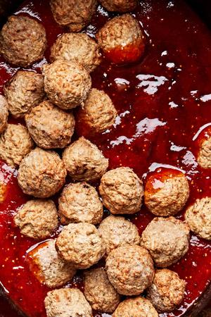 meatballs being stirred with fig jam, chili sauce and orange juice in a slow cooker