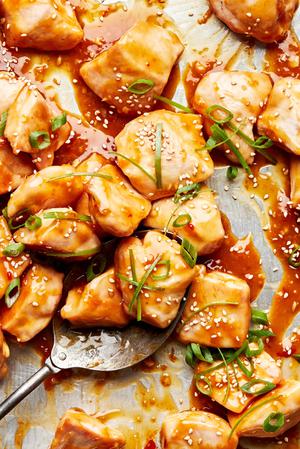 homemade orange chicken on a baking sheet sprinkled with sesame seeds and green onions