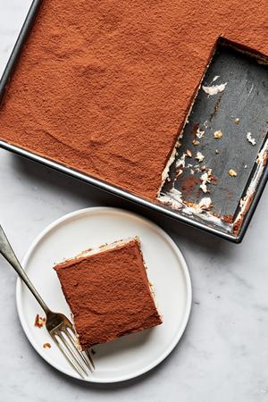 tiramisu being sliced made with coffee soaked lady fingers, layered with spiced whipped cream and topped with cocoa powder