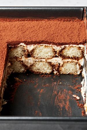 tiramisu being sliced made with coffee soaked lady fingers, layered with spiced whipped cream and topped with cocoa powder