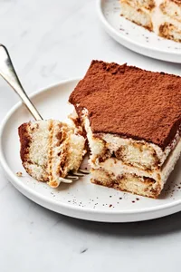 A slice of  easy tiramisu on a white plate, topped with spiced whipped cream, and a dusting of cocoa powder.