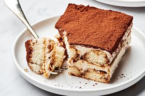 A slice of easy tiramisu on a white plate, topped with spiced whipped cream, and a dusting of cocoa powder.