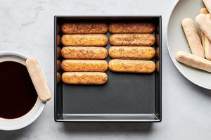 Ladyfingers dipped in espresso being arranged in a pan to layer for tiramisu.