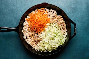 carrots, cabbage and spices being added to a skillet of cooked ground turkey