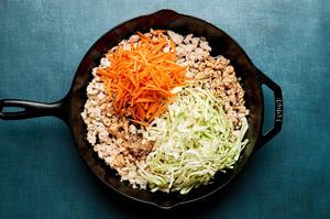 carrots, cabbage and spices being added to a skillet of cooked ground turkey