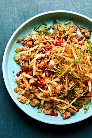 egg roll in a bowl drizzled with sriracha and sprinkled with wonton strips, green onions and sesame seeds