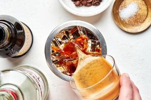 an espresso martini being poured over ice into a cocktail shaker made with vodka, Kahlua, espresso and salt