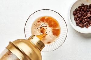 an espresso martini being poured from a cocktail shaker into a martini glass next to a bowl of coffee beans for garnishing