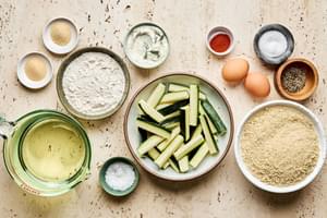 Ingredients for crispy fried zucchini: zucchini, flour, breadcrumbs, eggs, garlic powder & seasonings arranged on a counter