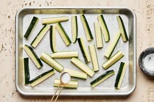 zucchini cut into spears being sprinkled with salt ton a baking dish to extract moisture