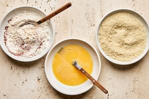 a bowl of beaten eggs, a bowl of panko and a bowl of flour mixed with spices to bread zucchini