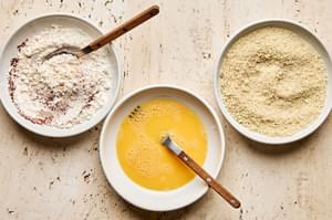 a bowl of beaten eggs, a bowl of panko and a bowl of flour mixed with spices to bread zucchini