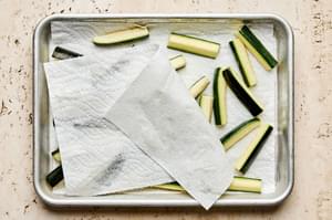 salted zucchini spears being patted dry with a paper towel