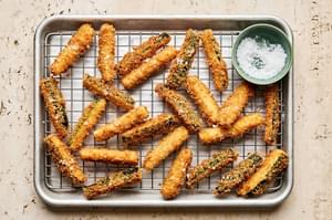 Extra crispy panko crusted fried zucchini spears being sprinkled with flaky salt cooling on a metal cooling rack.