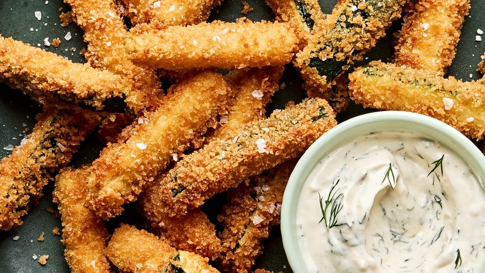 Golden-brown, extra crispy fried zucchini sticks sprinkled with flaky salt served with a side of creamy dill dip.