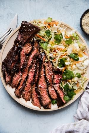 thin slices of grilled flank steak marinated in hoisin and five spice next to an asian salad on a plate