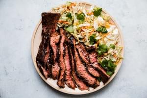 thin slices of grilled flank steak marinated in hoisin and five spice next to an asian salad on a plate