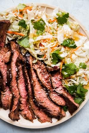 thin slices of grilled flank steak marinated in hoisin and five spice next to an asian salad on a plate