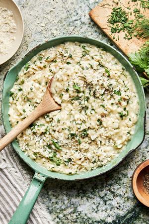 homemade fresh herb risotto made with butter, parmesan, garlic, shallots and lemon in a pot with a wooden spoon