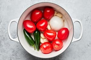 tomatoes, jalapeños, white onion and garlic being charred in a skillet