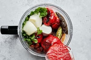 charred vegetables, crushed tomatoes, cilantro, salt and white onion being blended in a food processor