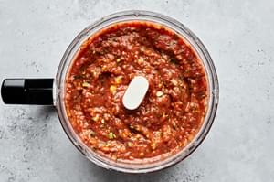 homemade salsa in a food processor made with charred vegetables, crushed tomatoes, cilantro, salt, onion and avocado