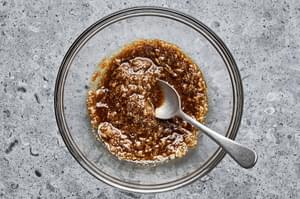 marinade in a glass bowl with a spoon made with salt, garam masala, garlic, ginger, olive oil, and brown sugar.