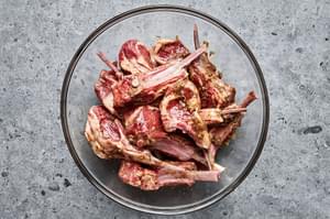 lamb chops in a bowl marinating with salt, garam masala, garlic, ginger, olive oil, and brown sugar.