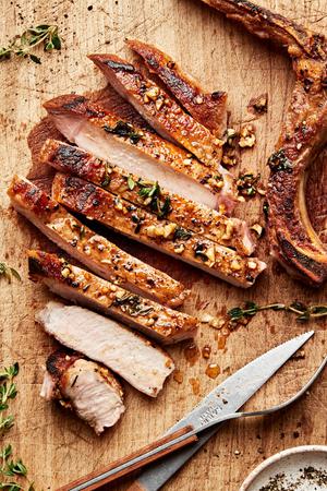 garlic butter pork chops seasoned with salt, pepper, garlic and thyme being sliced on a cutting board
