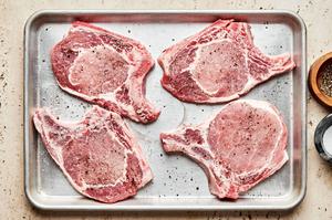 4 raw bone-in pork chops on a baking sheet seasoned with salt and pepper