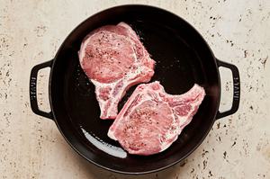 2 bone-in pork chops pork chops seasoned with salt and pepper being cooked in a skillet with vegetable oil