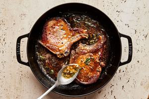garlic butter pork chops in a skillet with melted herb butter being spooned over the top