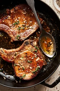 garlic butter pork chops in a skillet with melted herb butter being spooned over the top