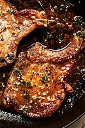 garlic butter pork chops in a skillet seasoned with salt, pepper, garlic and thyme