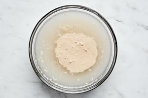 instant dry yeast being sprinkled over warm water in a glass bowl